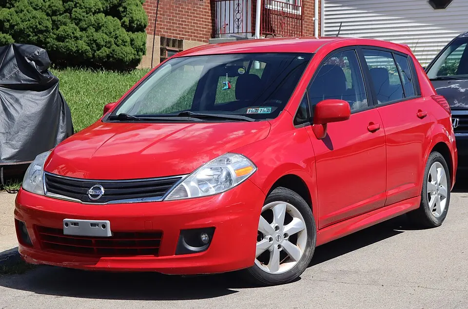 2012 Nissan Versa 1.8 SL hatchback in Red Alert Metallic, front left, 09-06-2026, photographed in United States
